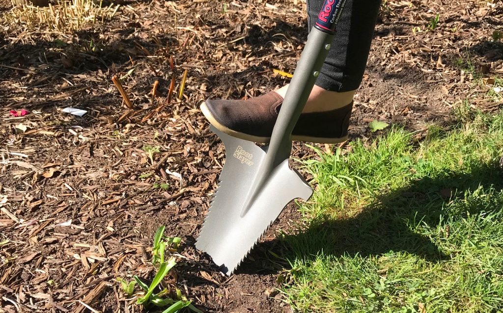 A person is seen applying foot pressure to a Radius Garden root slayer in order to dig up soil