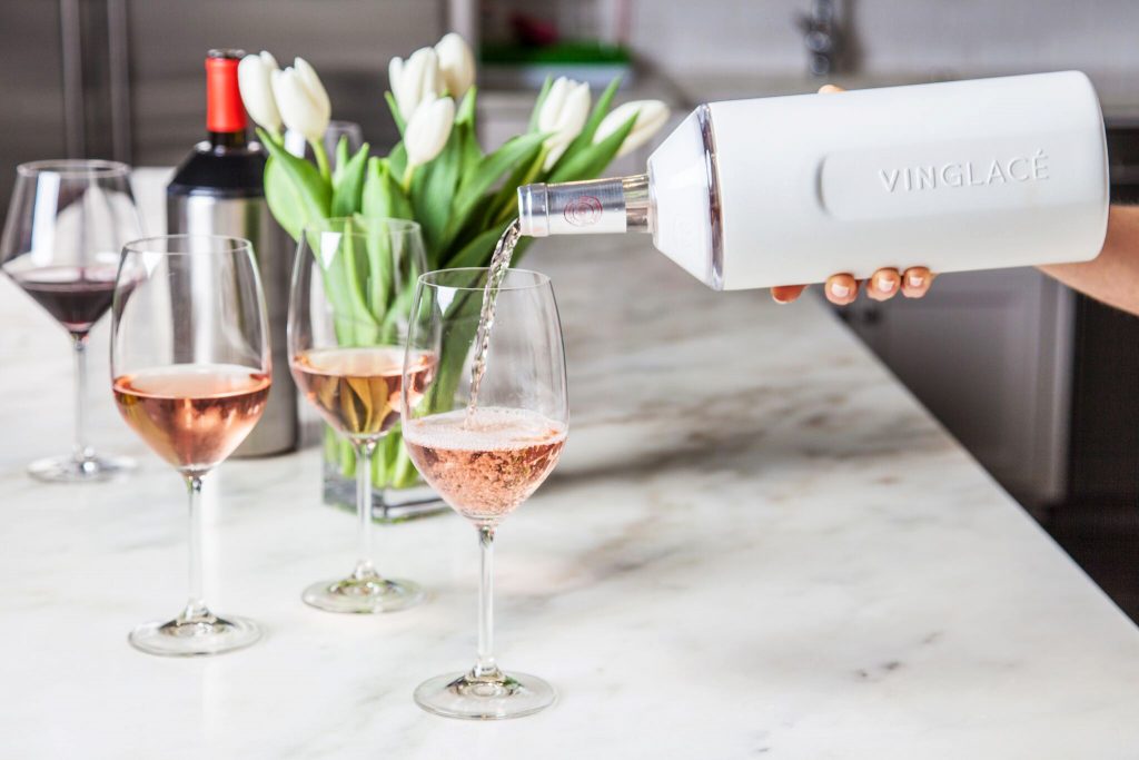 A woman pours rose from a Vinglace stainless steel wine chiller into wine glasses