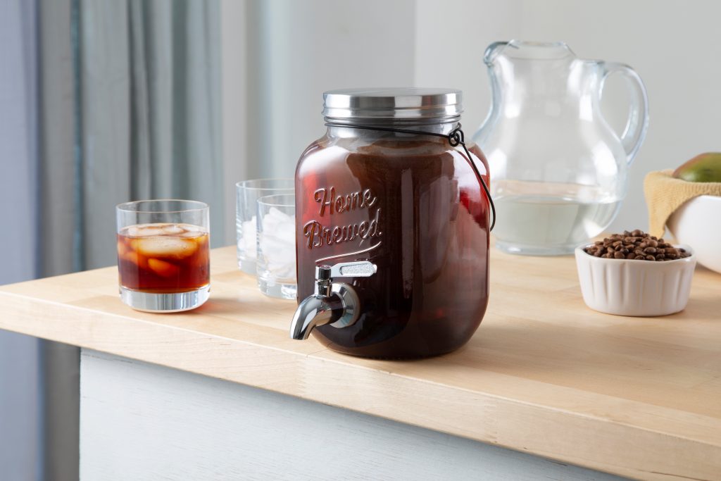 A glass jug of cold brew coffee sits on a counter, being pour from Willow & Everett's Cold Brew On Tap 2.0