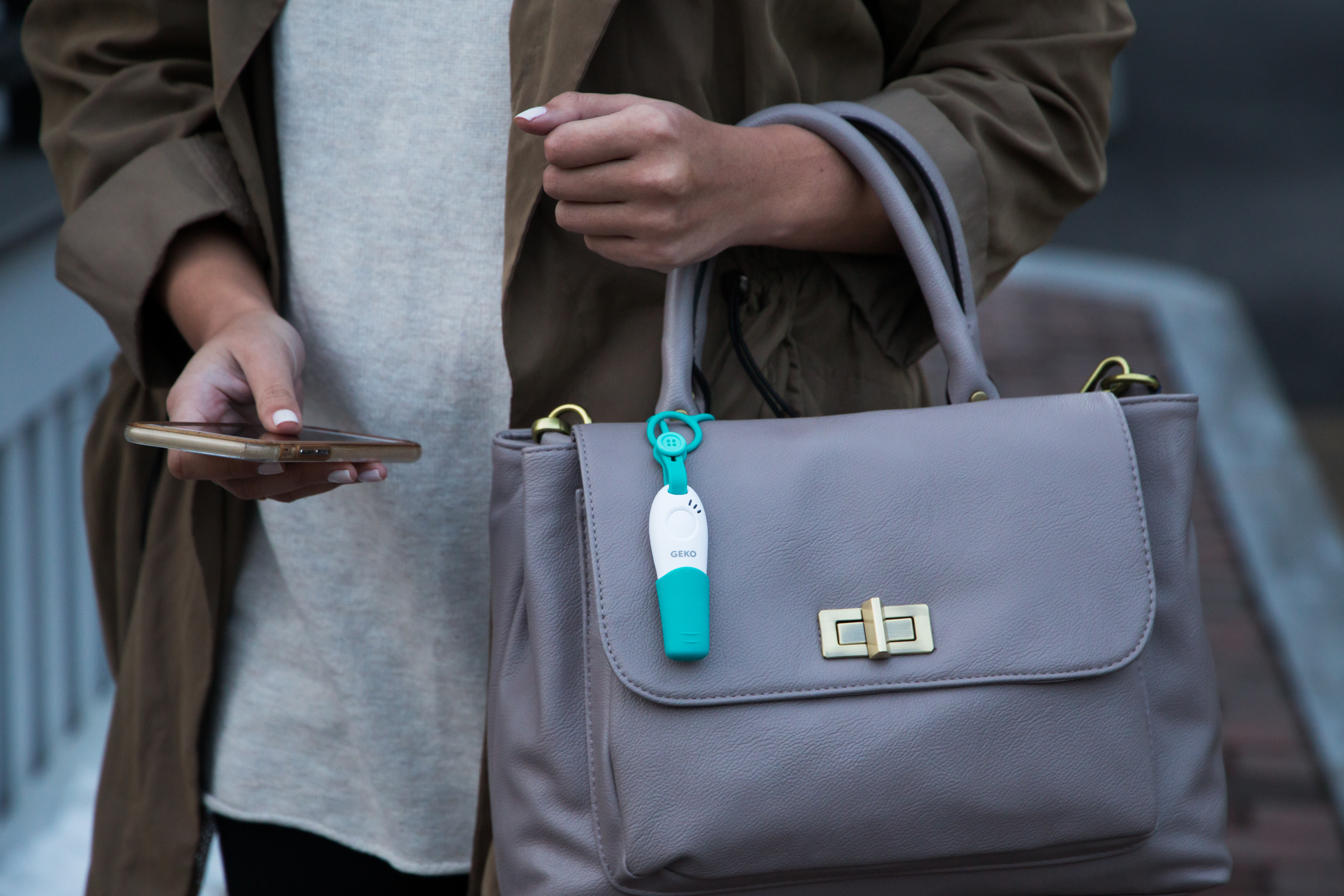 A teal & white GEKO safety whistle is strapped to a woman's purse