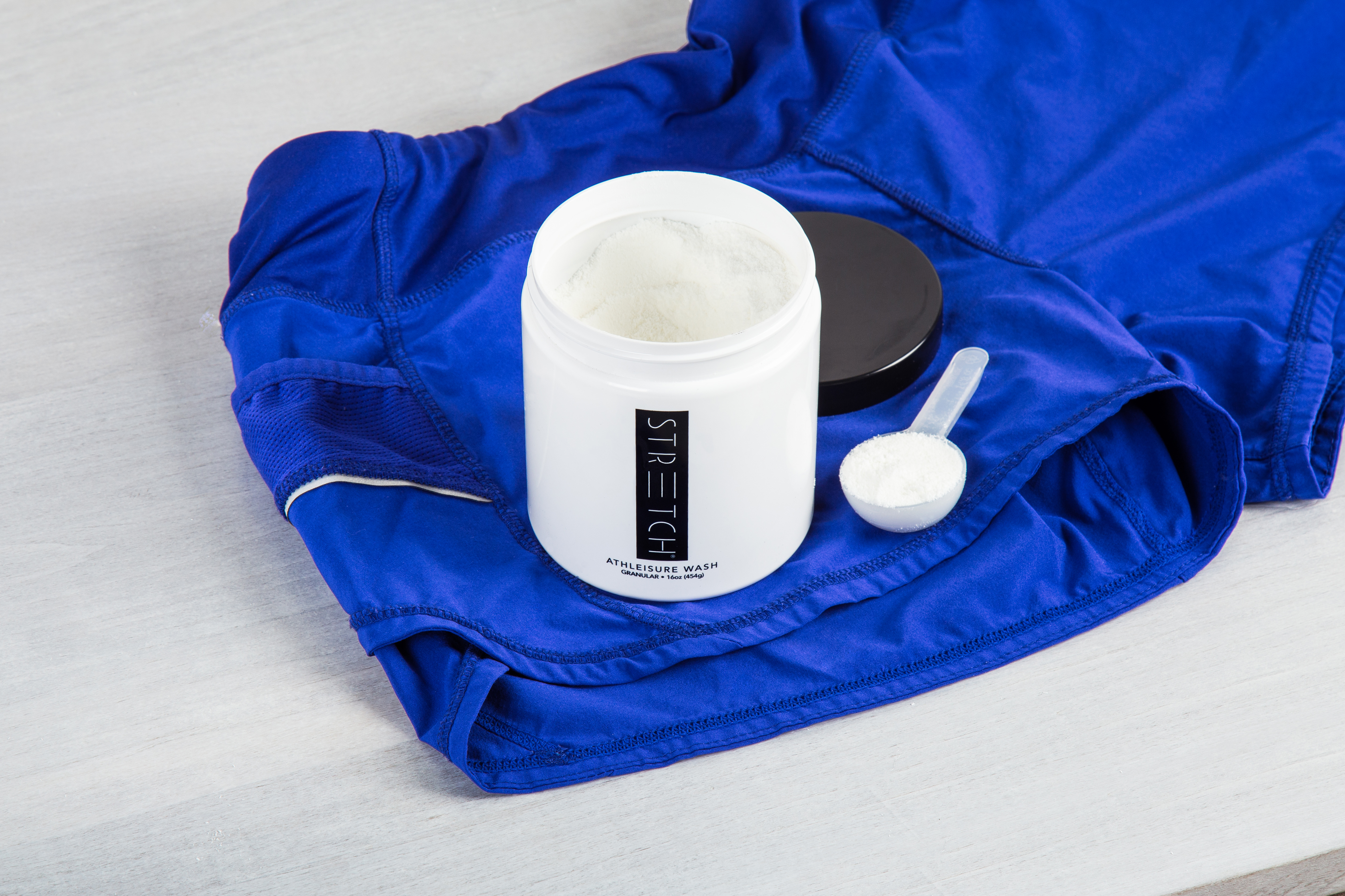 A jar of STRETCH activewear laundry detergent sits atop blue workout gear