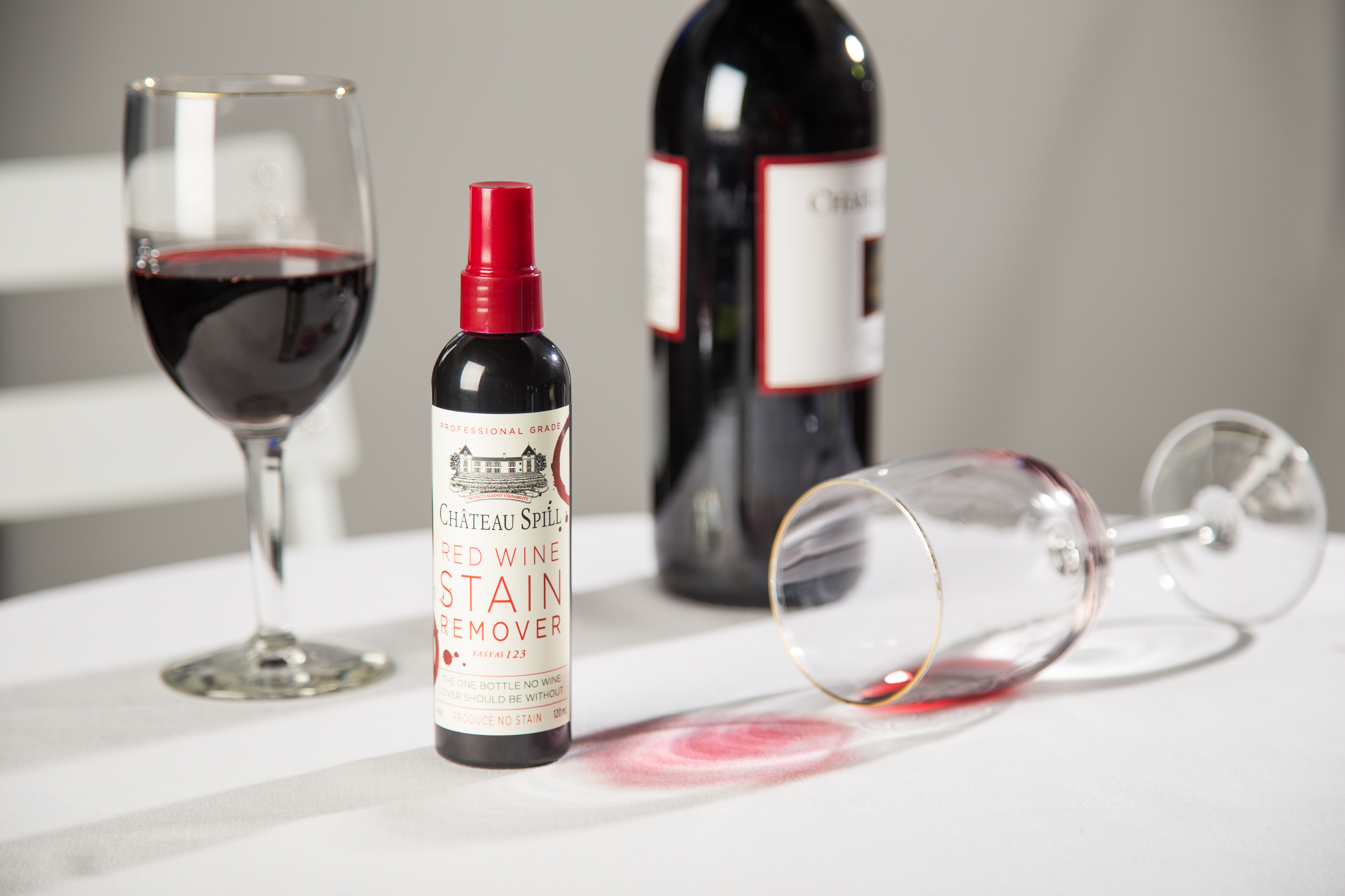 A bottle of Chateau Spill Red Wine Stain Remover sits on a tablecloth stained with red wine