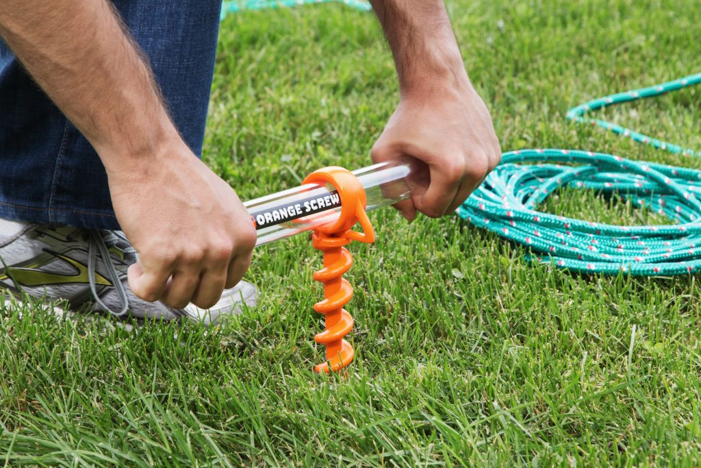 A man screws giant orange screws into the grass for anchoring rope