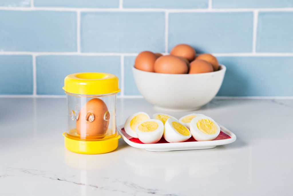 Perfectly peeled hard boiled eggs sit on a plate next to Negg, the easy hard boiled egg peeler