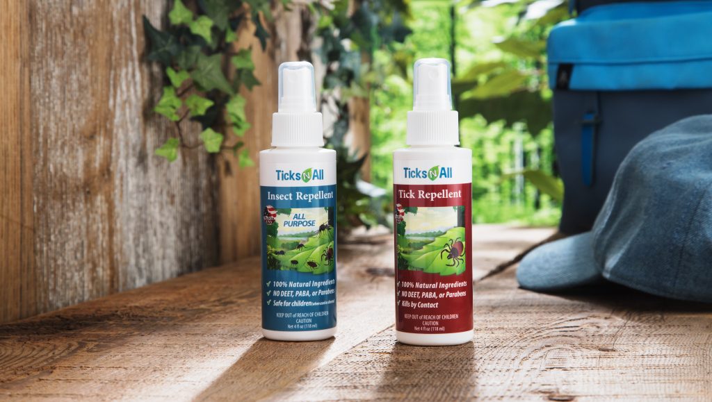 Tick & Insect repellant spray bottles from Ticks-N-All sit on a wood patio