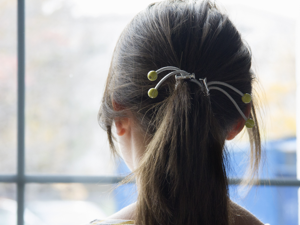 A girl keeps her ponytail in place with a white & green tennis version of Sporteez' sliding hair ties