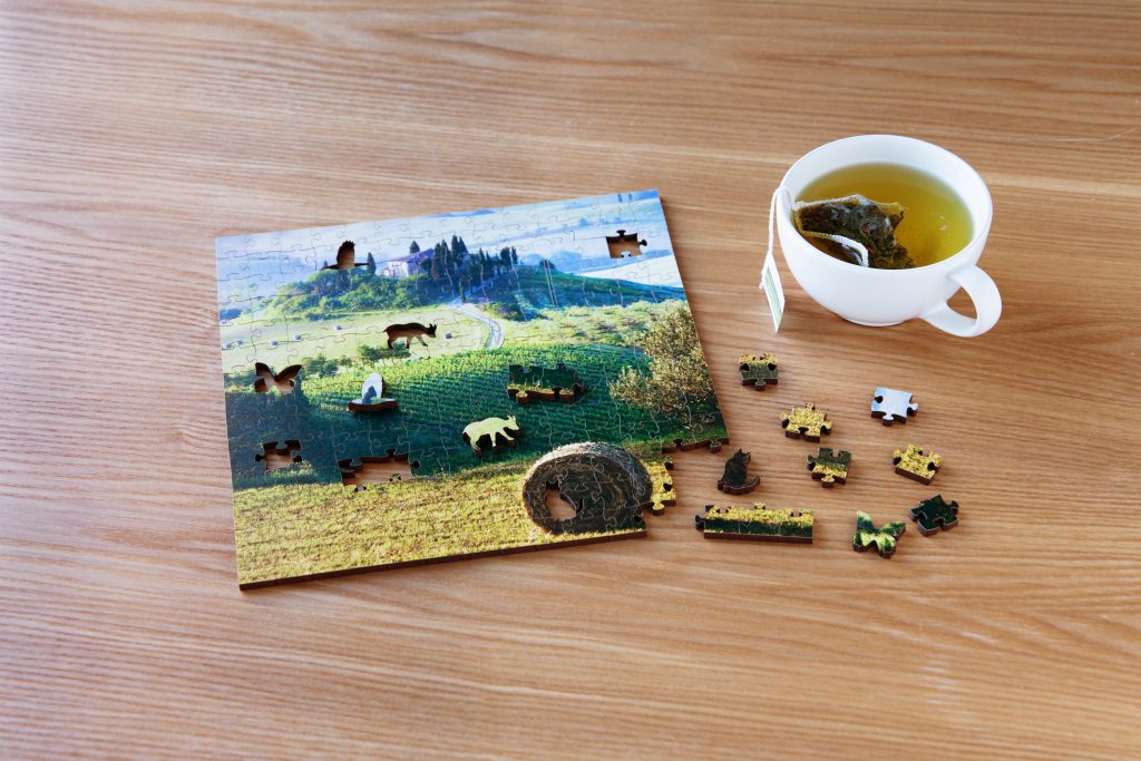  A mostly finished wooden jigsaw puzzle depicting a field scene from Zen Art & Design sits on a coffee table next to a cup of tea