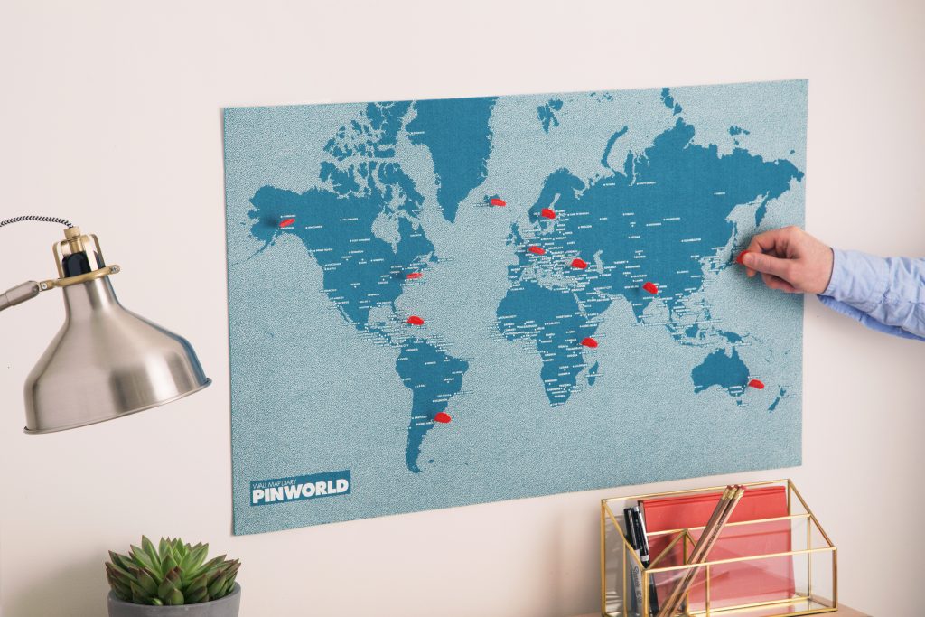 A man places a pin on his blue Palomar felt world map to mark his travels 