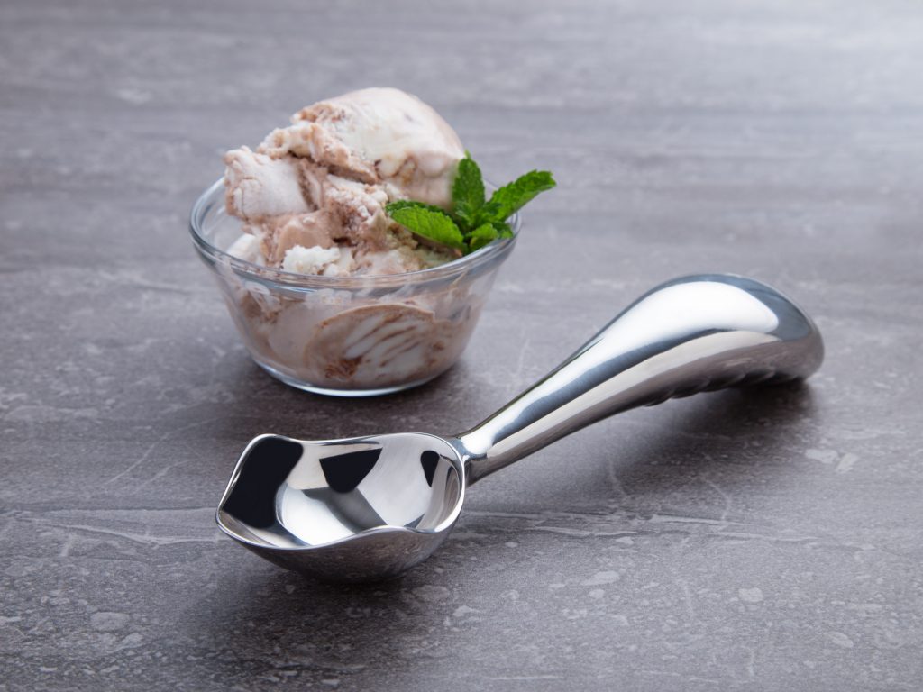 A bowl of ice cream sits next to Midnight Scoop's ergonomic ice cream scooper