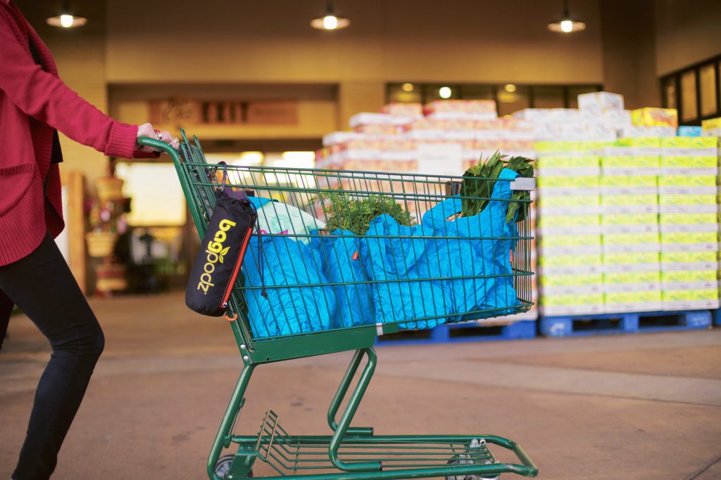 A woman pushes a shopping cart with blue reusable BagPods holding her groceries