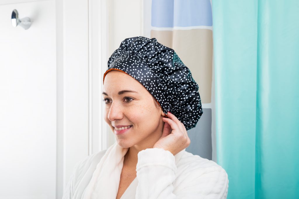 A woman is seen getting out of the shower wearing a black TIARA shower cap