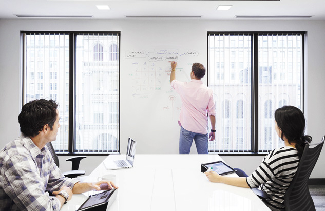 A man is seen writing on the wall of a conference room during a meeting using IdeaPaint's whiteboard paint