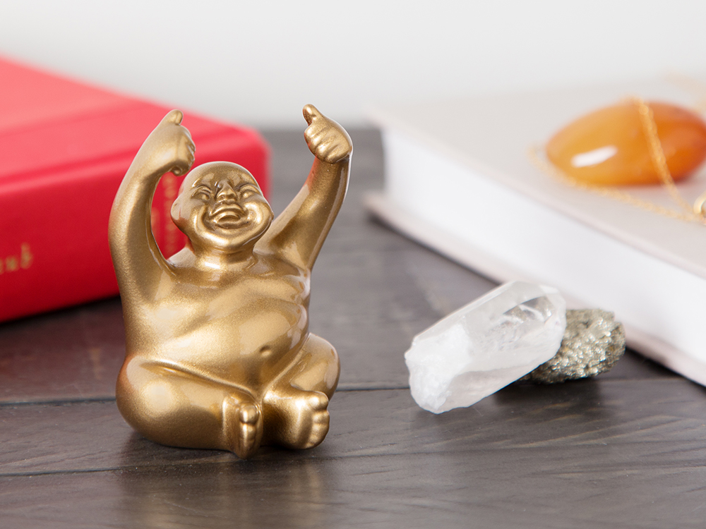 A miniature gold smiling monk figurine from Suburban Monk sits on a desk