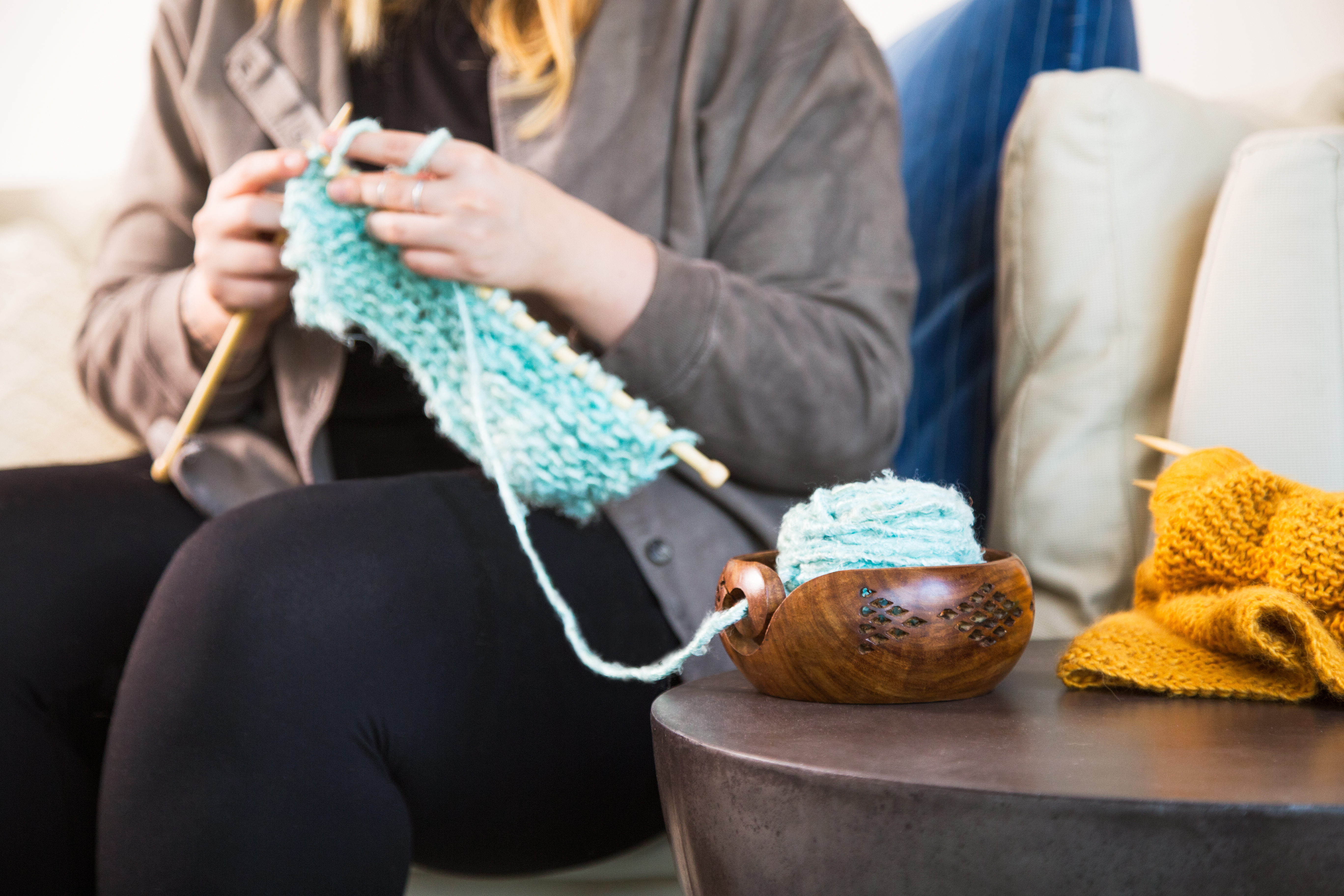 A woman is seen sitting and knitting using a Darn Good Yarn wooden yarn bowl