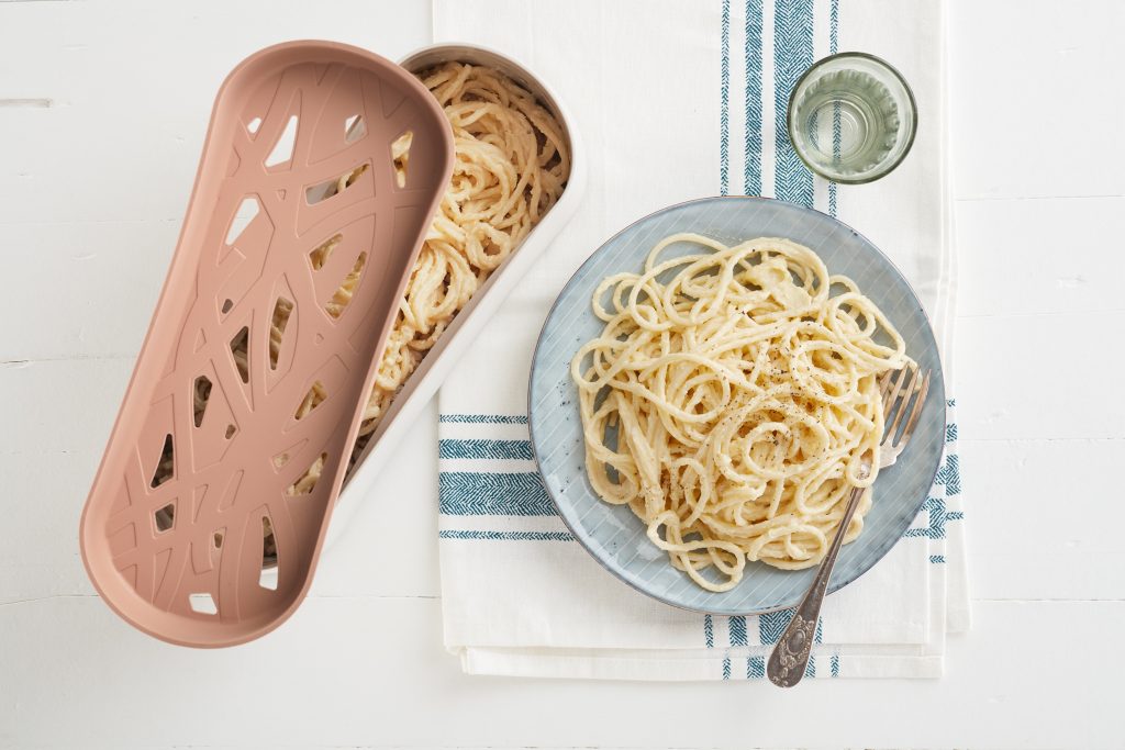 A plate of freshly cooked pasta sits next to Lékué's microwavable pasta cooker