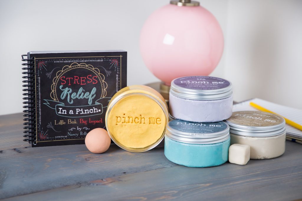 Several jars of pinch me therapy dough sit next to a stress relief book