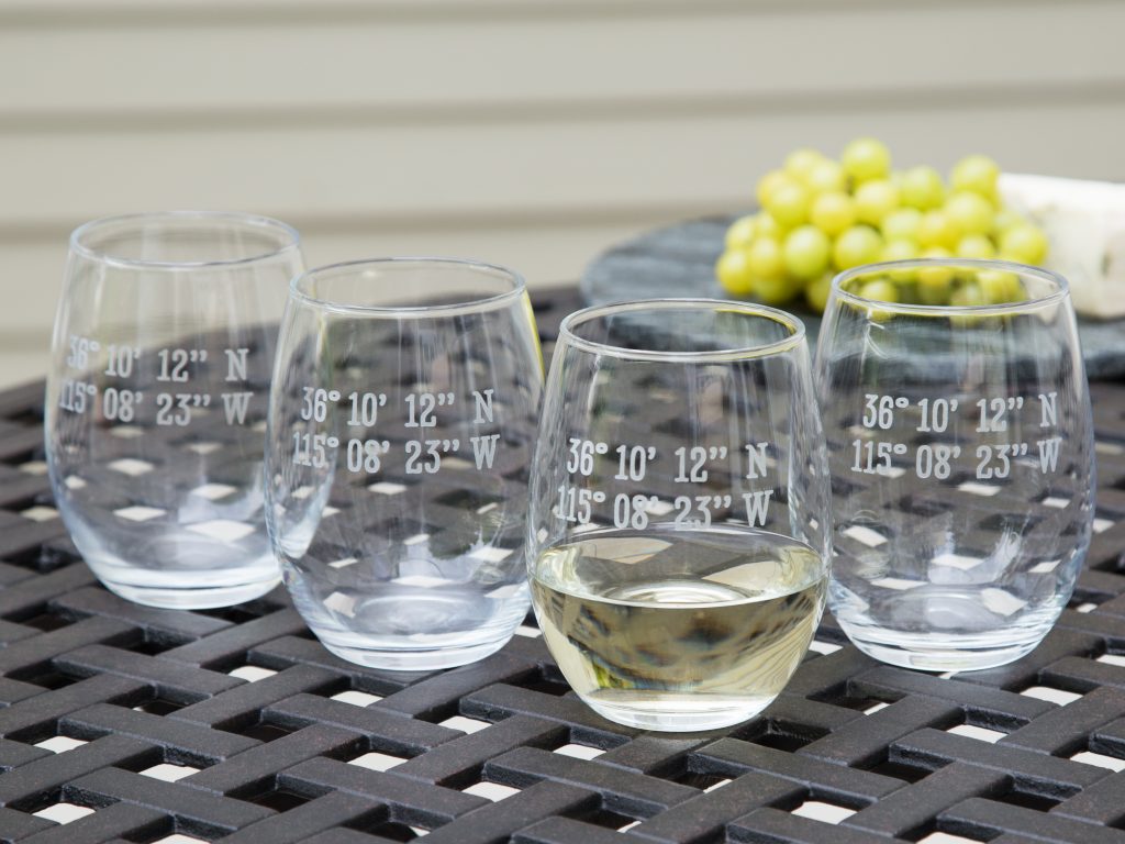 Four custom latitude & longitude stemless wine glasses from Susquehanna Glass Company sit on a patio table