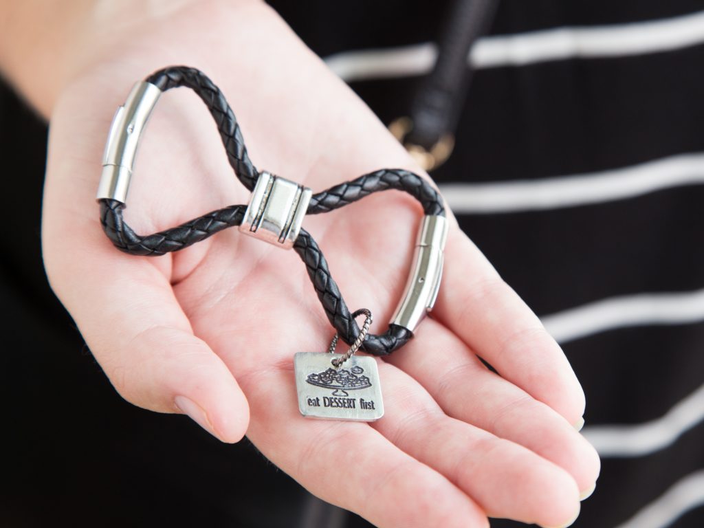 A My-Storytellers infinity loop keychain with a charm that says 'Eat dessert first' is seen in the palm of a woman's hand