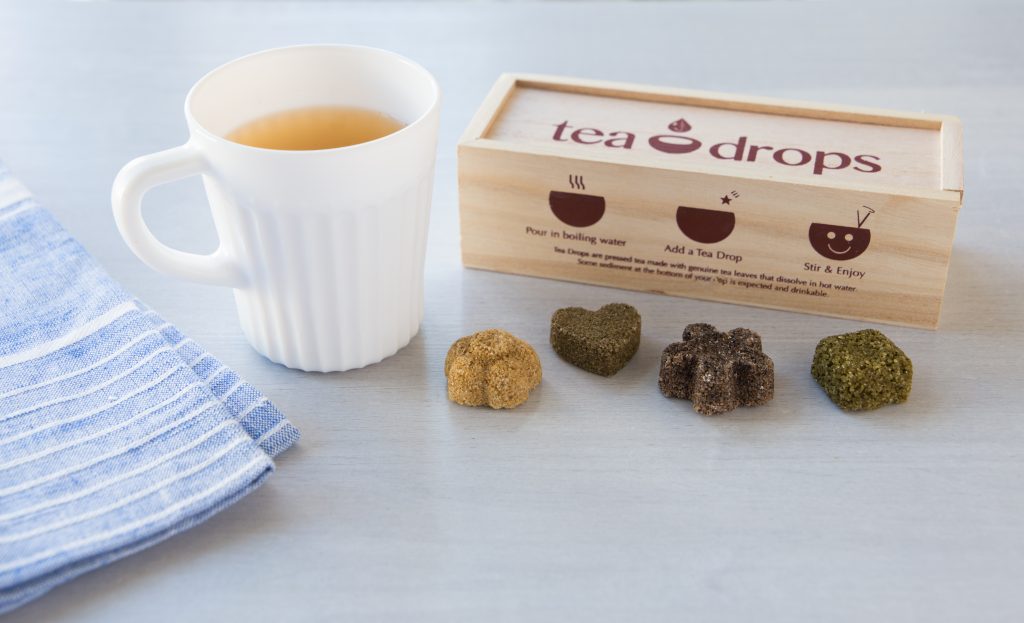 Four pressed Tea Drops sit on a counter next to a steaming cup of tea