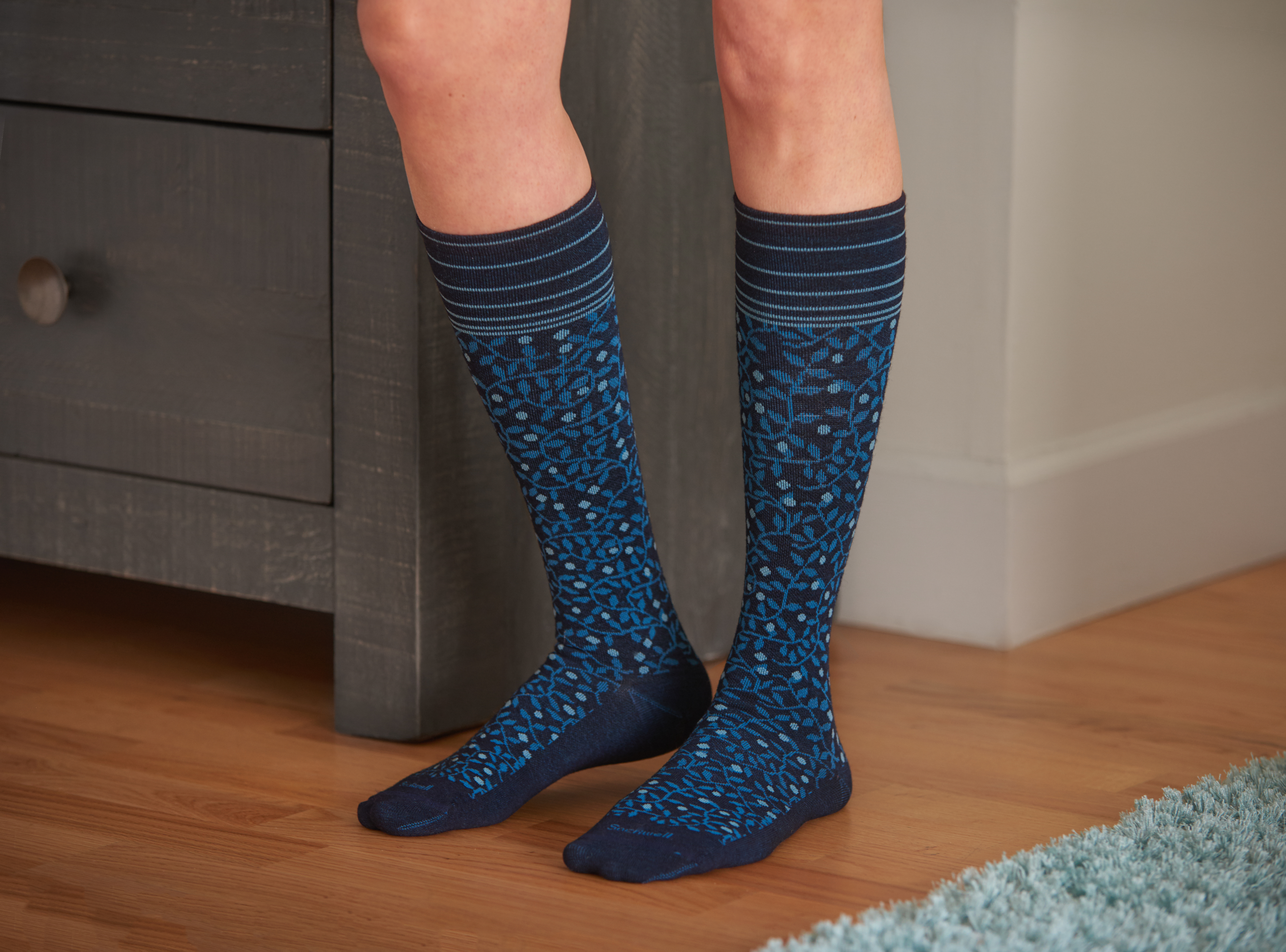 A woman is seen wearing a pair of navy printed tall, firm compression socks from Sockwell