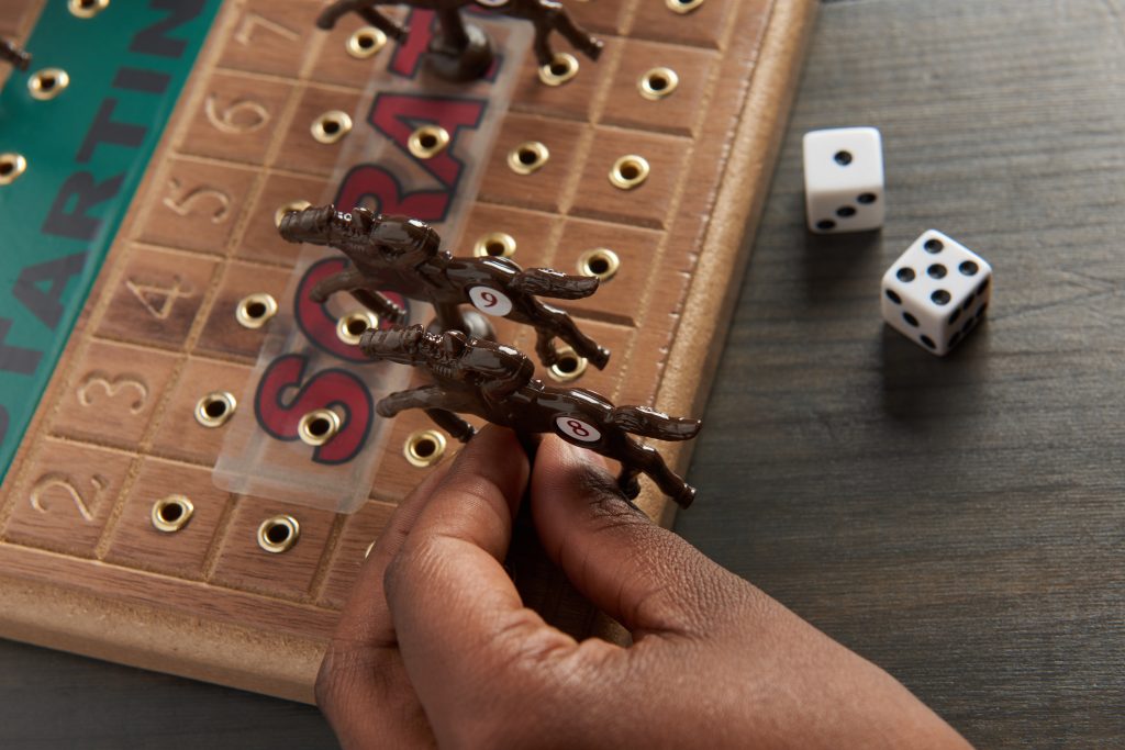 A person is seen playing a wooden tabletop horseracing game from Across The Board 