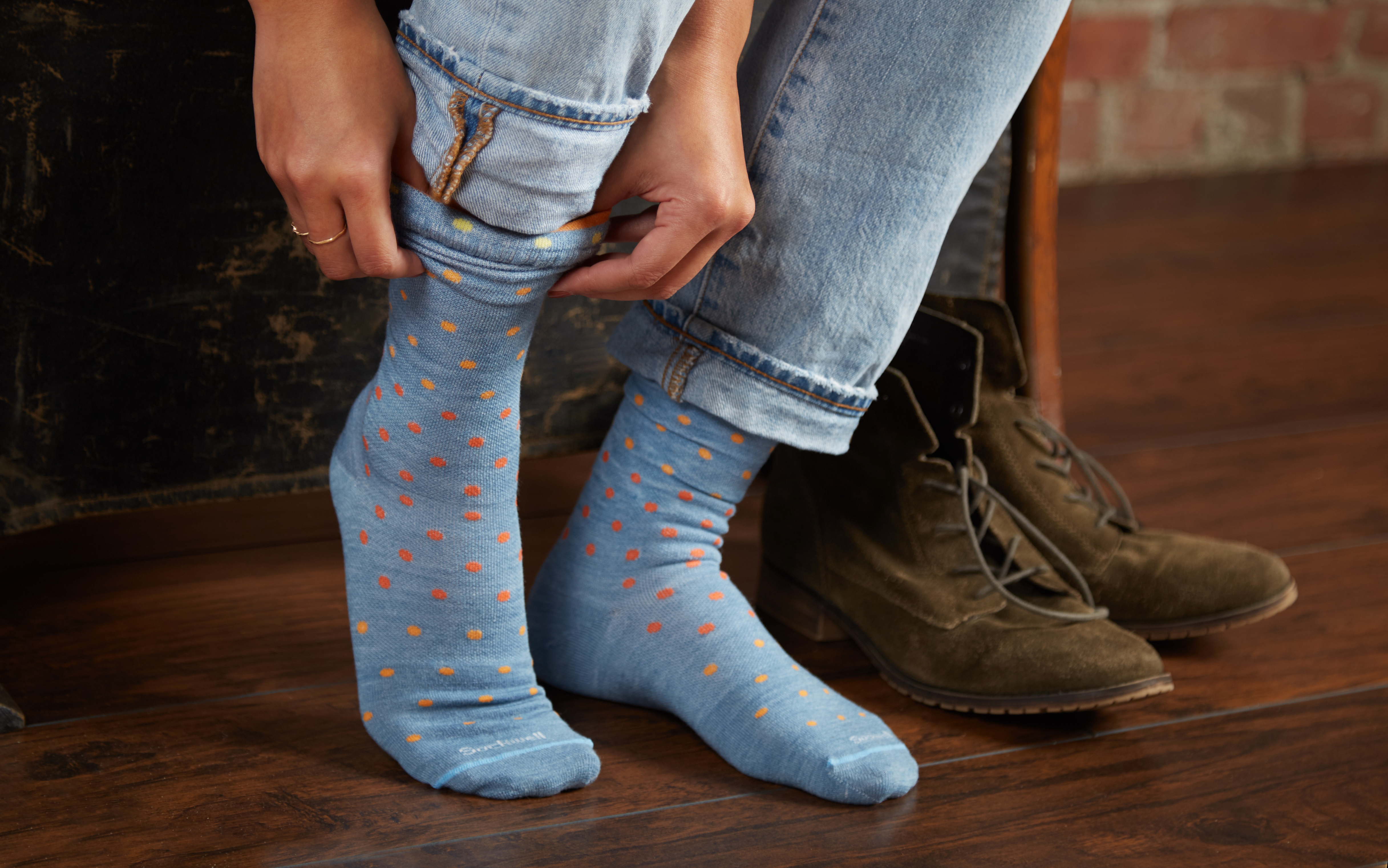 A woman is seen pulling on a pair of light blue polka dot medium compression socks from Sockwell