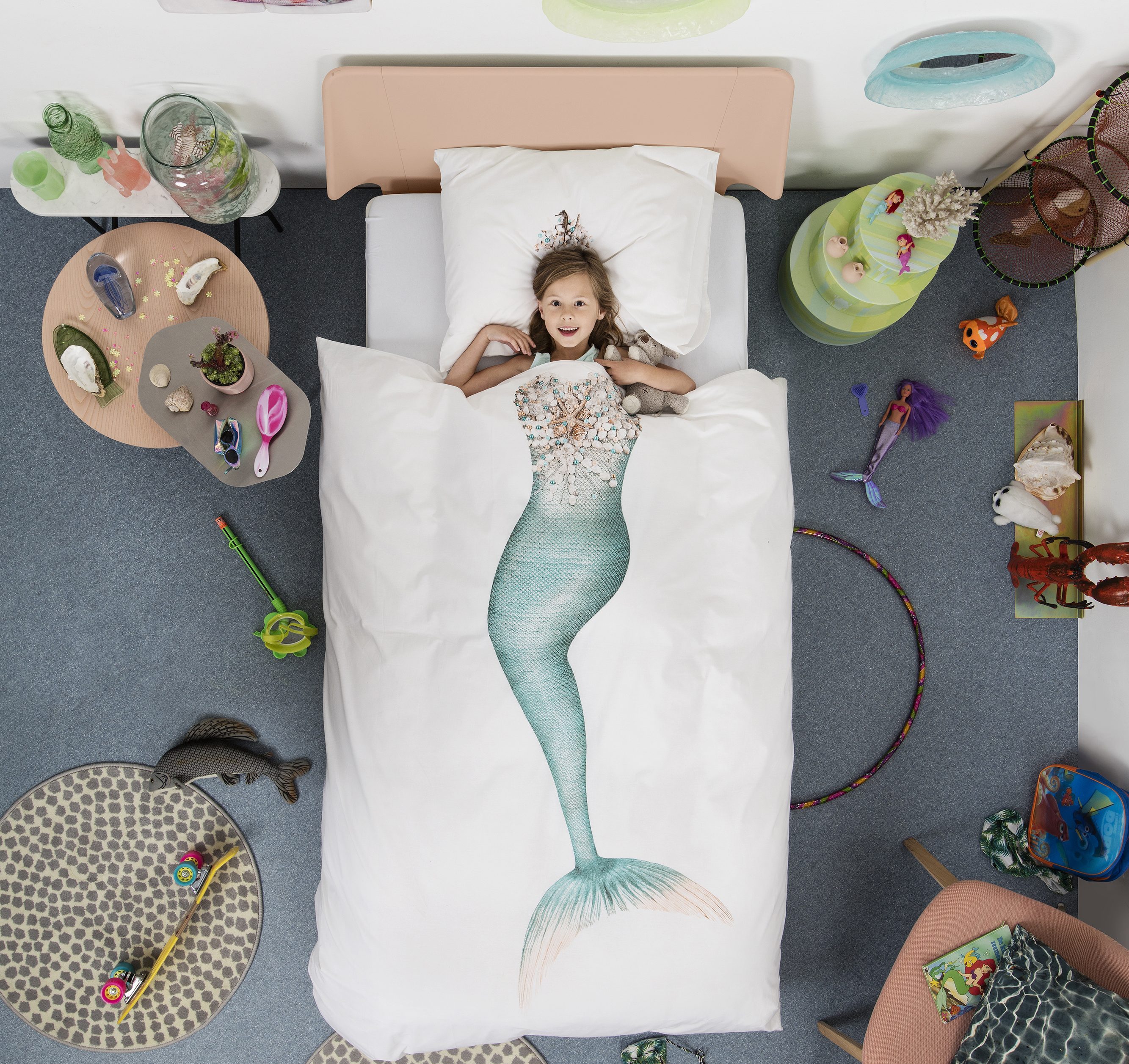 A little girl is seen laying in bed under a Mermaid duvet cover from Snurk Living