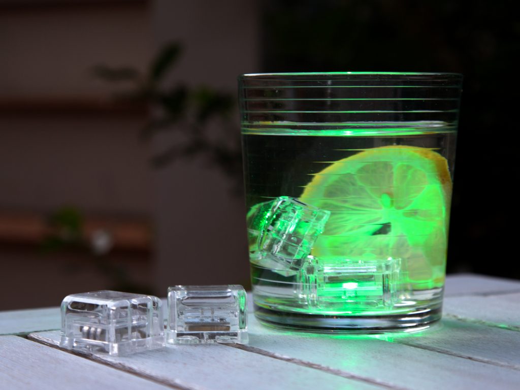 A cocktail with a lemon wheel is seen illuminated by glowing drink ice cubes from Glo Drinks
