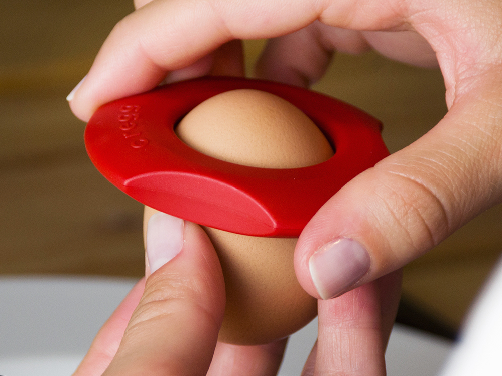 A person is seen using a red Cregg egg cutter to cut the top off their egg