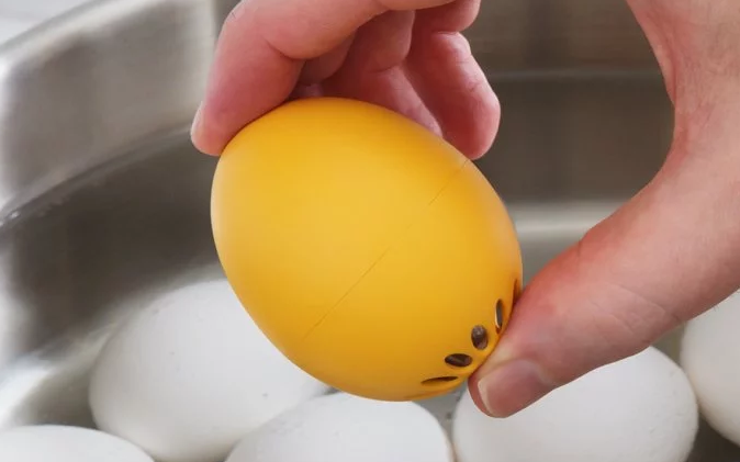 A yellow BeepEgg perfect egg timer is held above a pot of boiling water