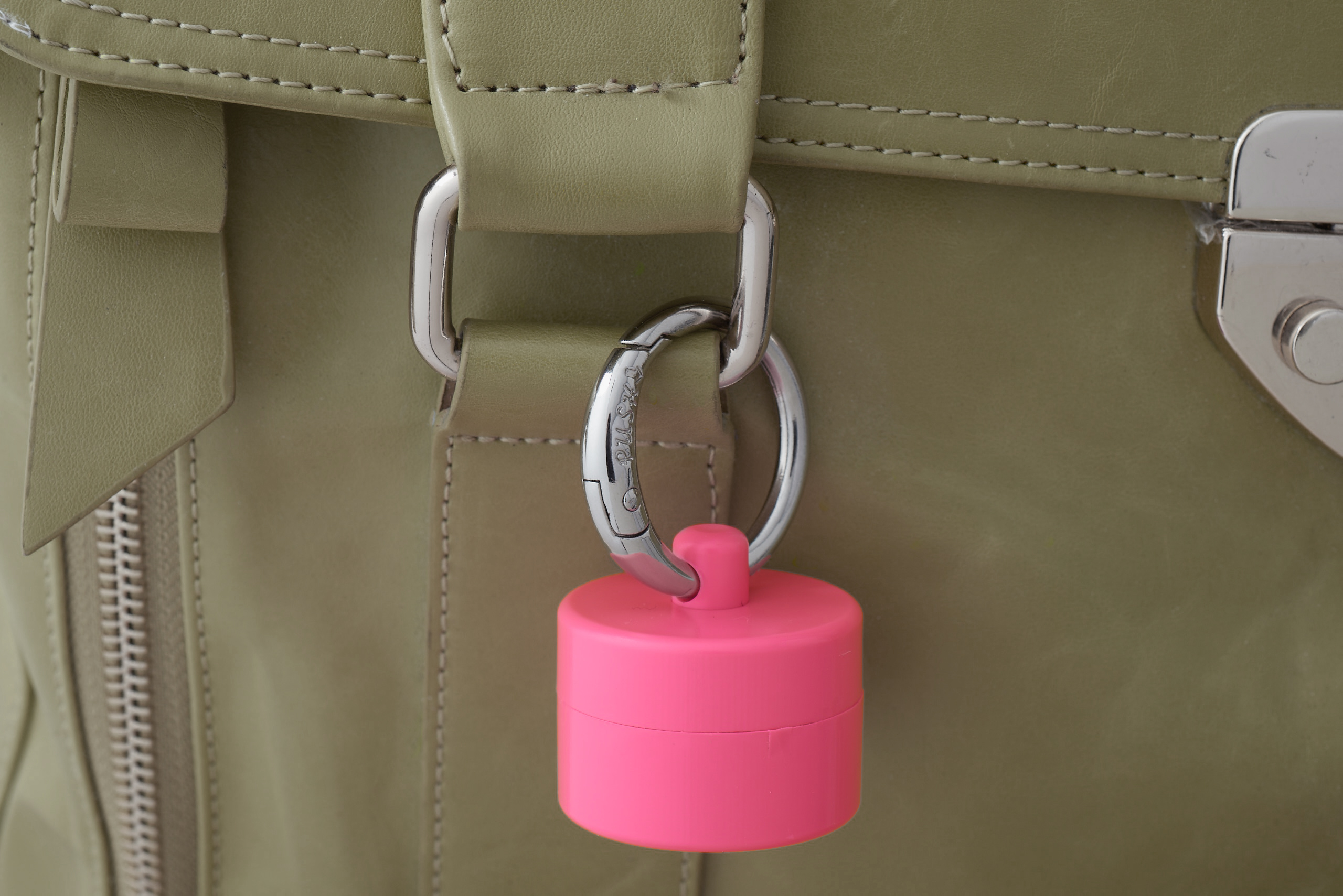 A pink Lion Latch keychain jewelry holder is seen clipped to a tan bag