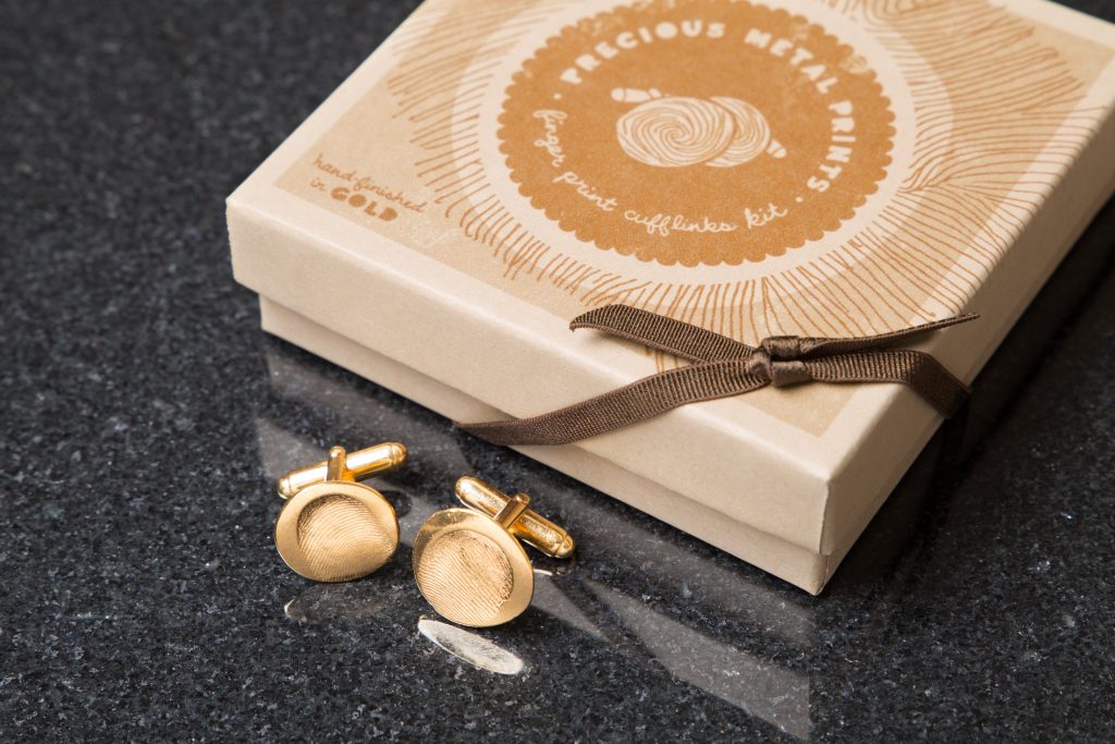 Two gold fingerprint cufflinks from Precious Metal Prints are seen next to a gift box