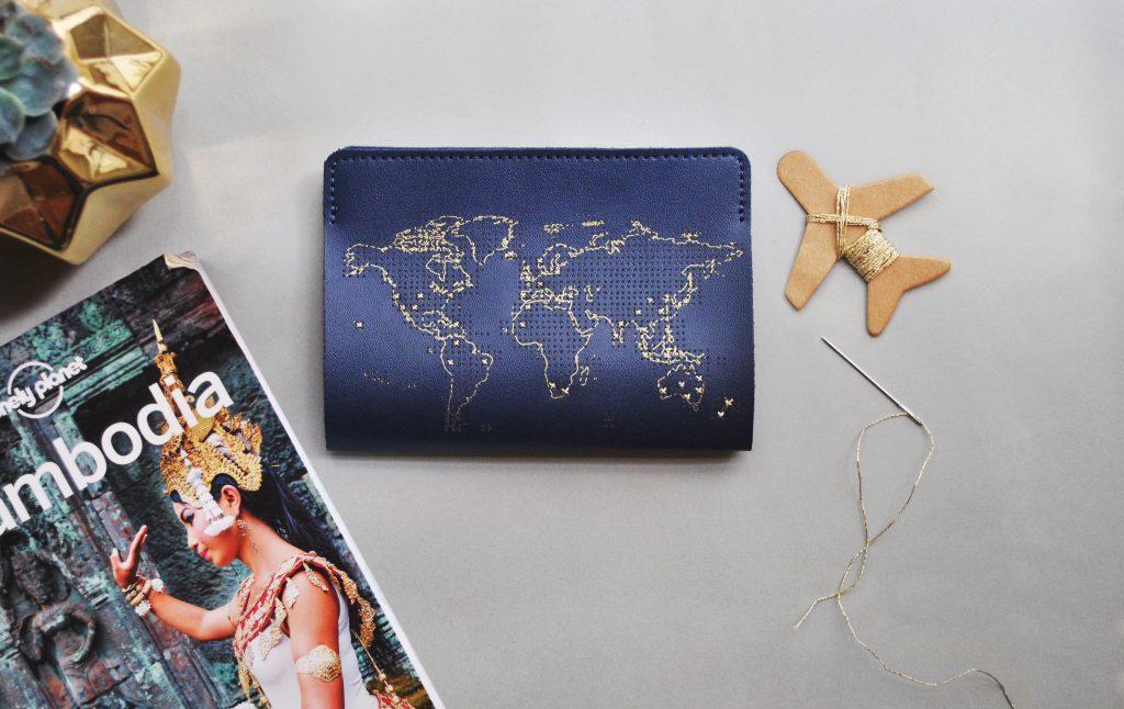 A navy stitched leather passport cover by Chasing Threads lays next to a needle & thread
