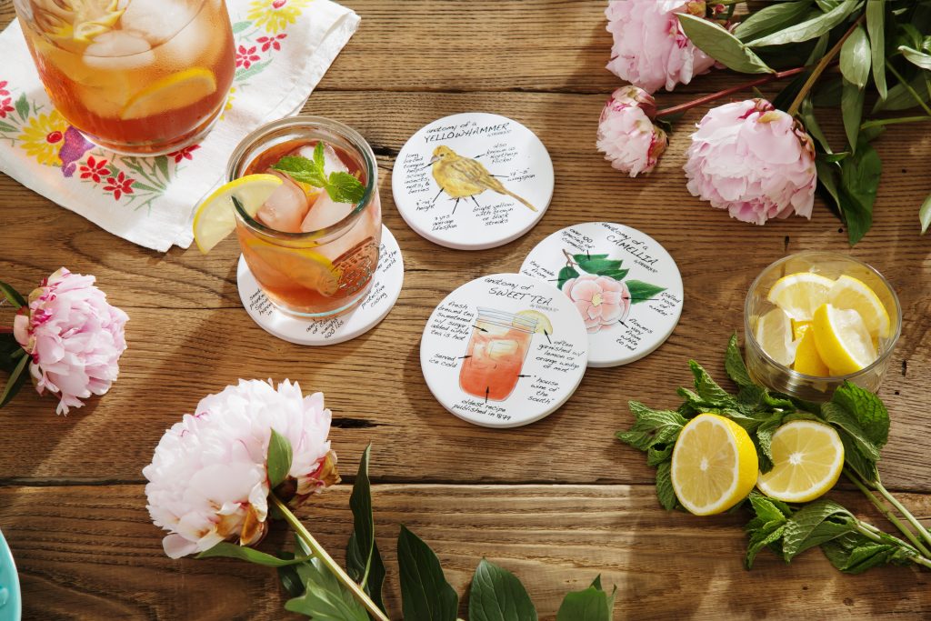A set of State-themed anatomy coasters from Dishique lay on a table with a pitcher of iced tea