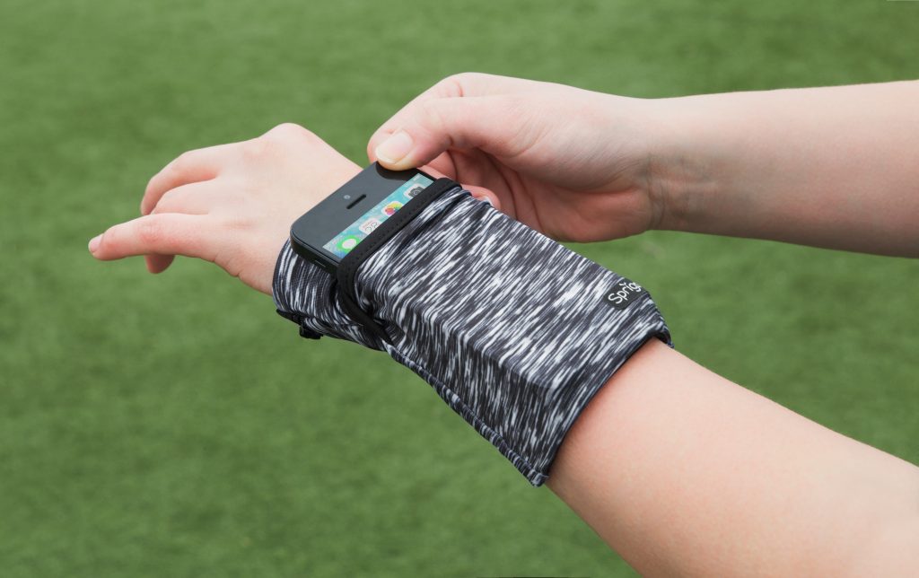 A person is seen pulling their phone out of a black Sprigs wristband wallet