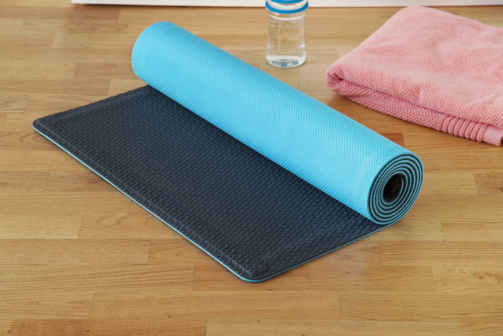 A blue and black YoYo self-rolling yoga mat lays next to a water bottle and towel