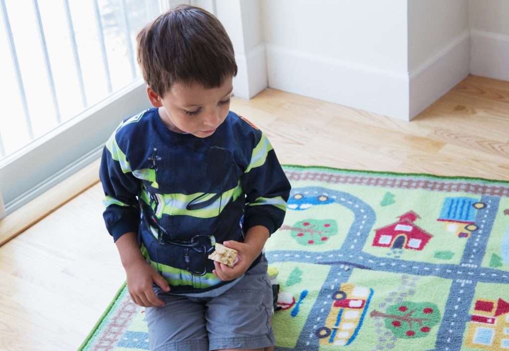 A little boy is seen playing on a town rug wearing a firefighter roleplaying bib from Mixed Pears