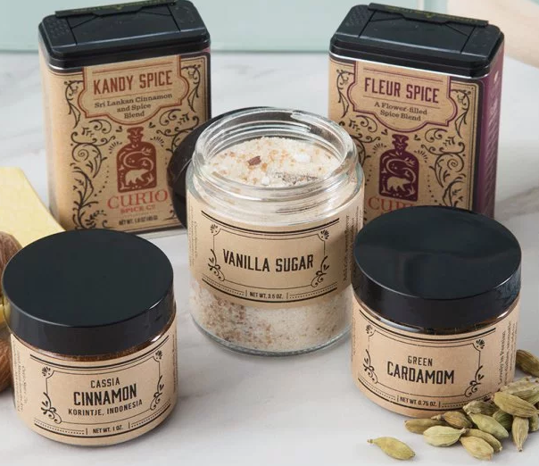 2 tins and 3 jars of baking spices from Curio Spice Co seen on a kitchen counter