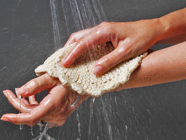 A woman can be seen washing her arms in the shower using a Toockies densely knit washcloth