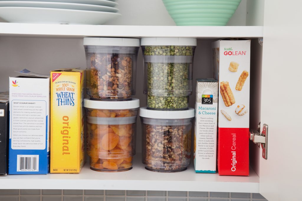 Four full Botto adjustable storage containers sit on a kitchen cabinet shelf next to cereal and crackers