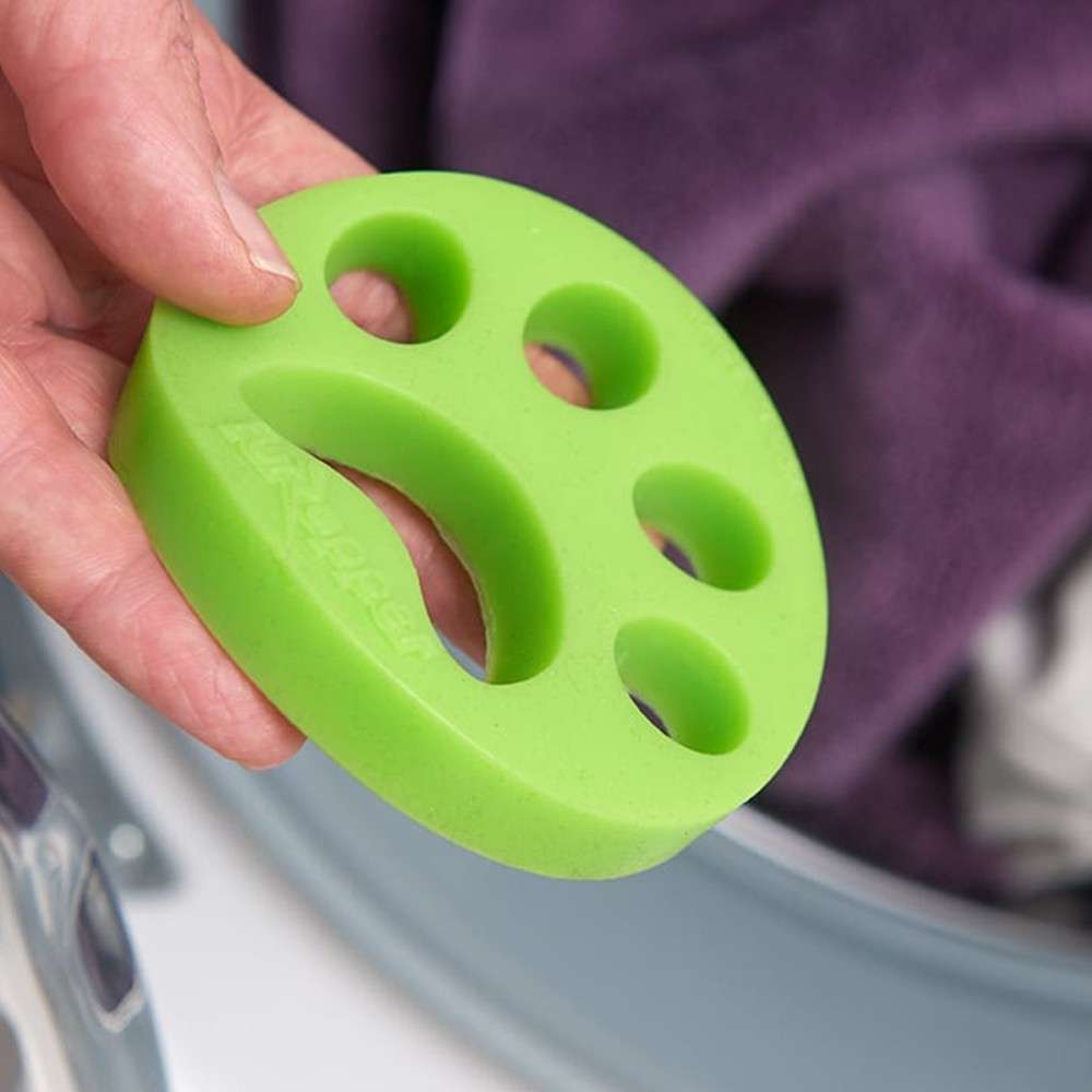 A green, paw print shaped disc being tossed into the washing machine.